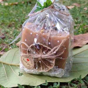 Vela aromática empaquetada sobre hojas verdes.