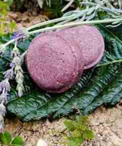 Jabón artesanal morado sobre hojas verdes y lavanda.